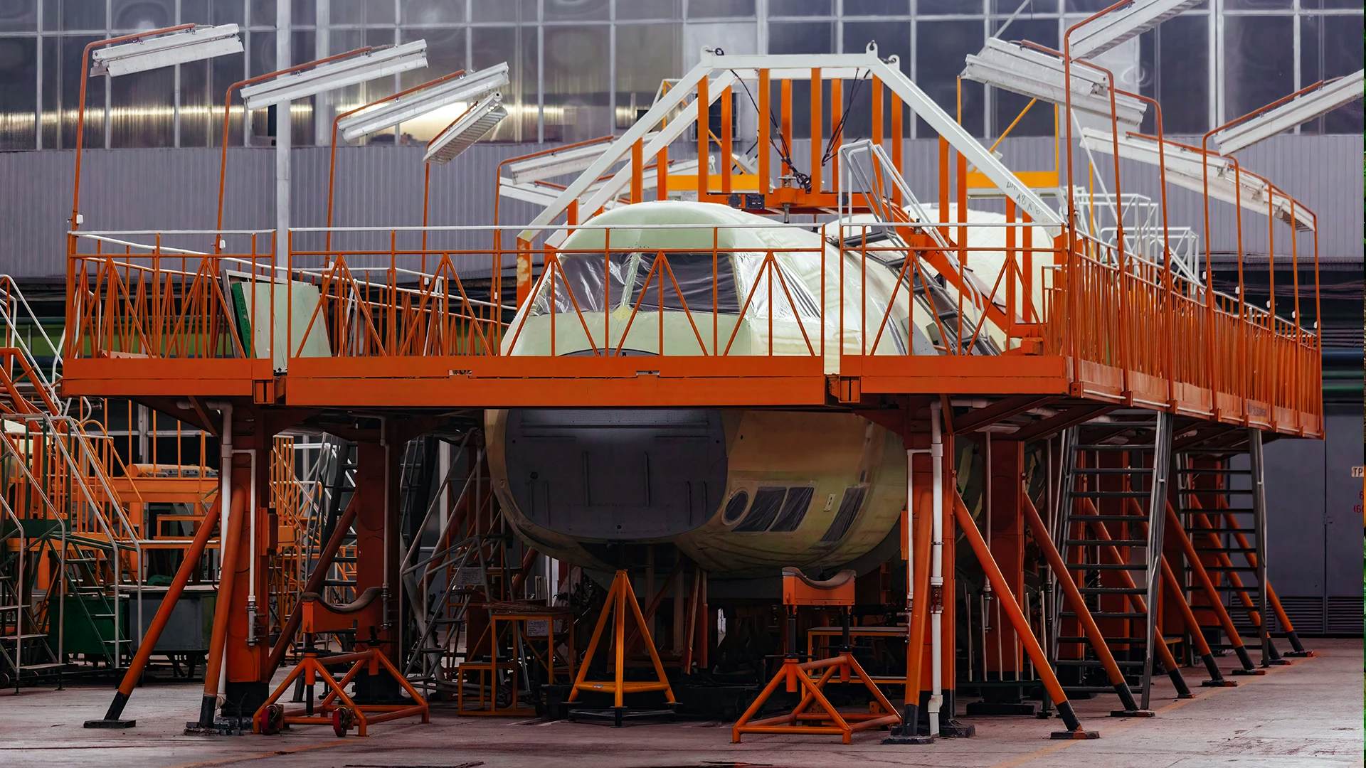 An aircraft under construction surrounded by scaffolding and support structures inside an industrial hangar.