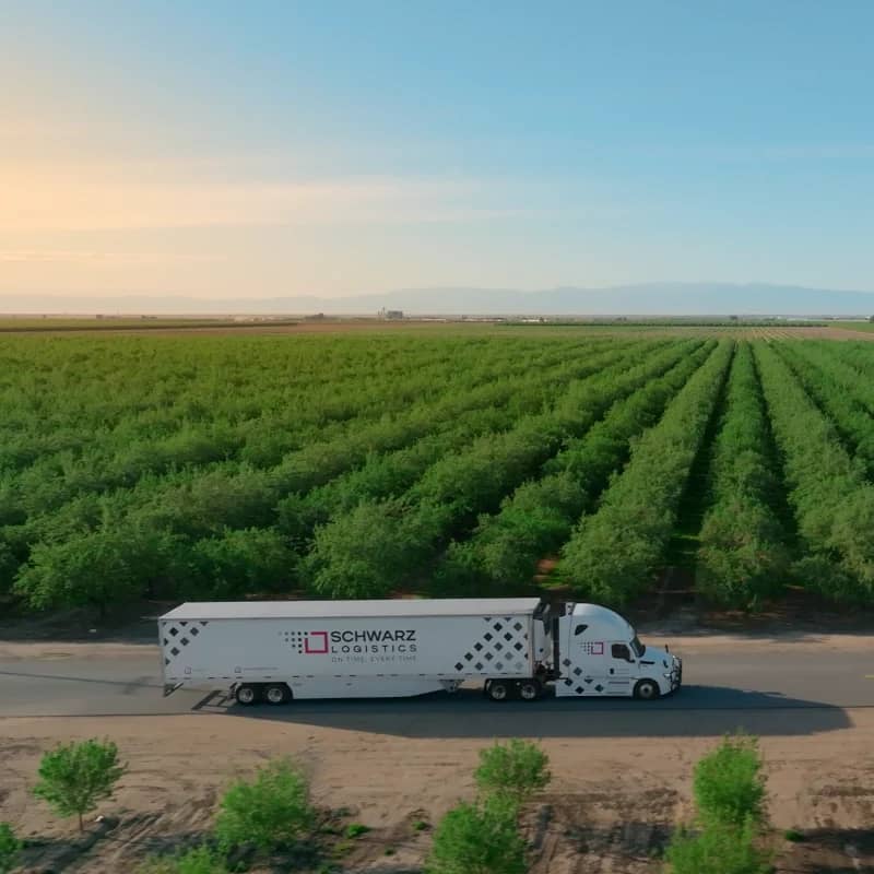 Schwarz Logistics truck driving by an orchard at dusk.