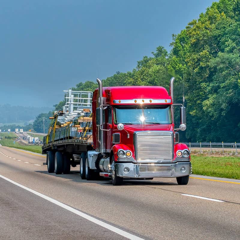 Red semi-truck transporting construction equipment on highway.