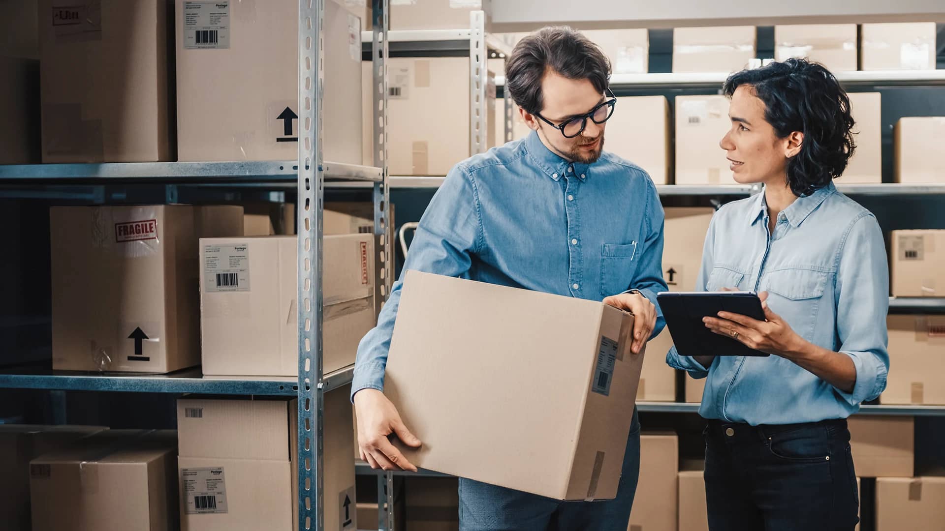 Two people with a clipboard and box in a storage room.