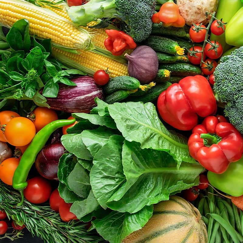 A vibrant, colorful display of fresh vegetables, including corn, tomatoes, cucumbers, broccoli, bell peppers, and lettuce.