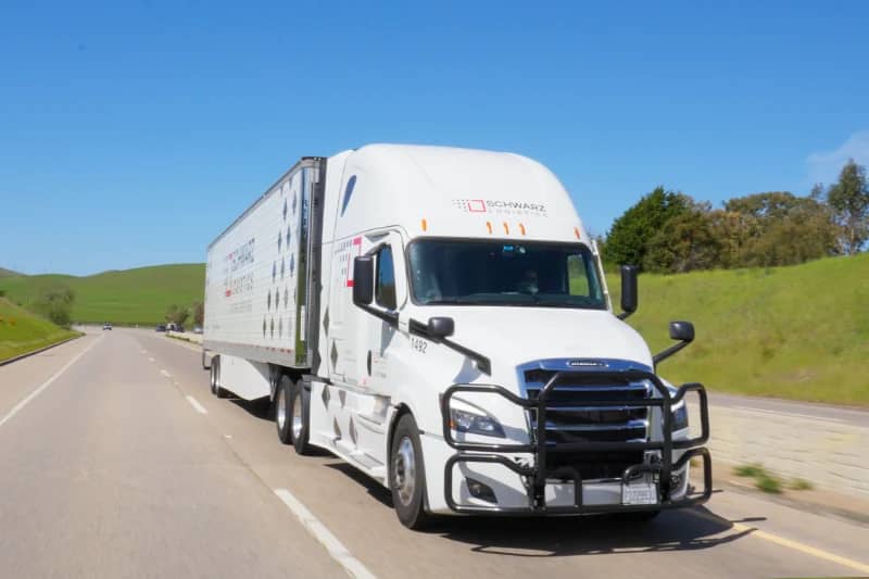 A white semi-truck with a trailer on a highway.