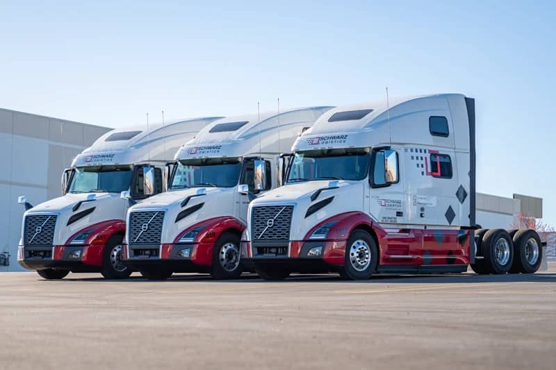 Three semi-trucks parked side by side at what appears to be a loading dock or a parking area for a logistics center.