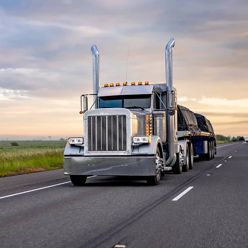 Silver flatbed truck on highway at dusk.