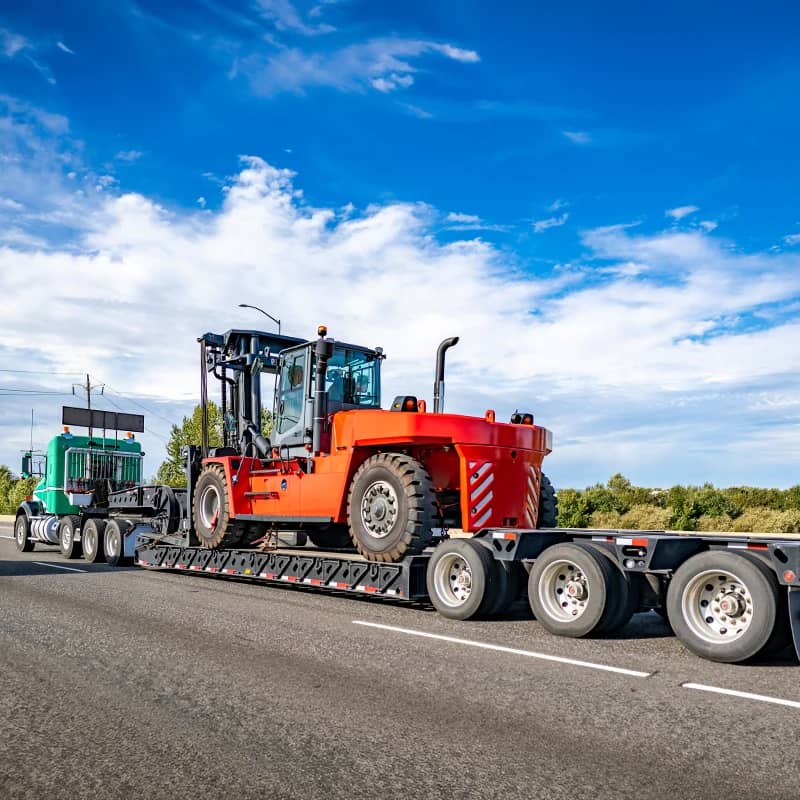 Semi hauling large orange machinery under blue skies.