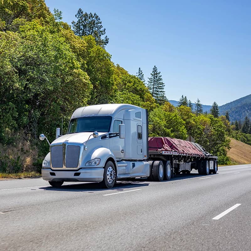 White semi truck with flatbed trailer on sunny road.