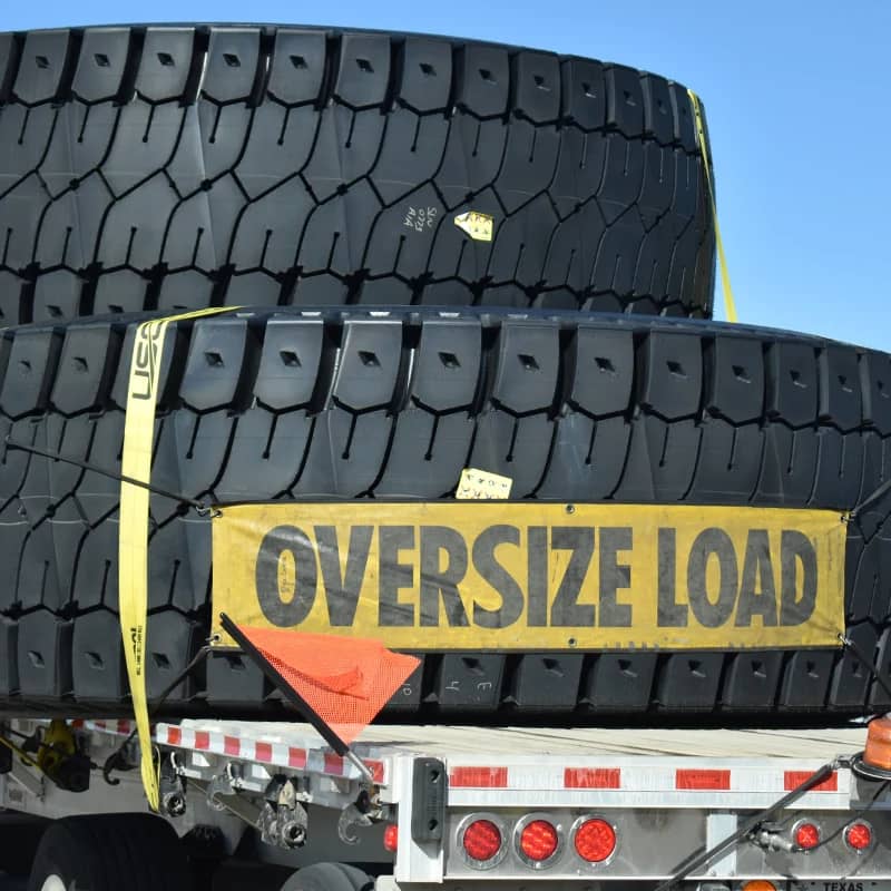 Trailer with stacked large tires and "OVERSIZE LOAD" sign.