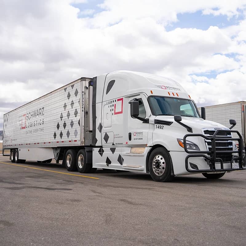 A parked semi-truck with a white cab and a large trailer, prominently featuring the logo of "SCHWARZ LOGISTICS" along with the slogan "ON TIME, EVERY TIME."