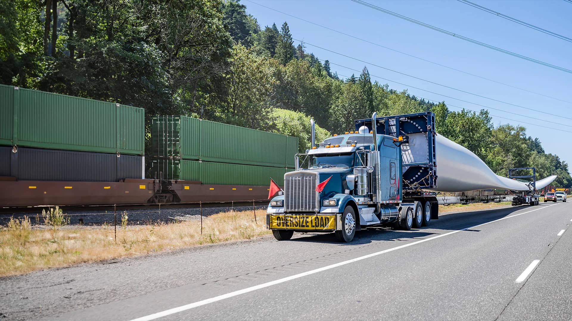 Truck with "Oversize Load" banner hauling wind turbine blade.