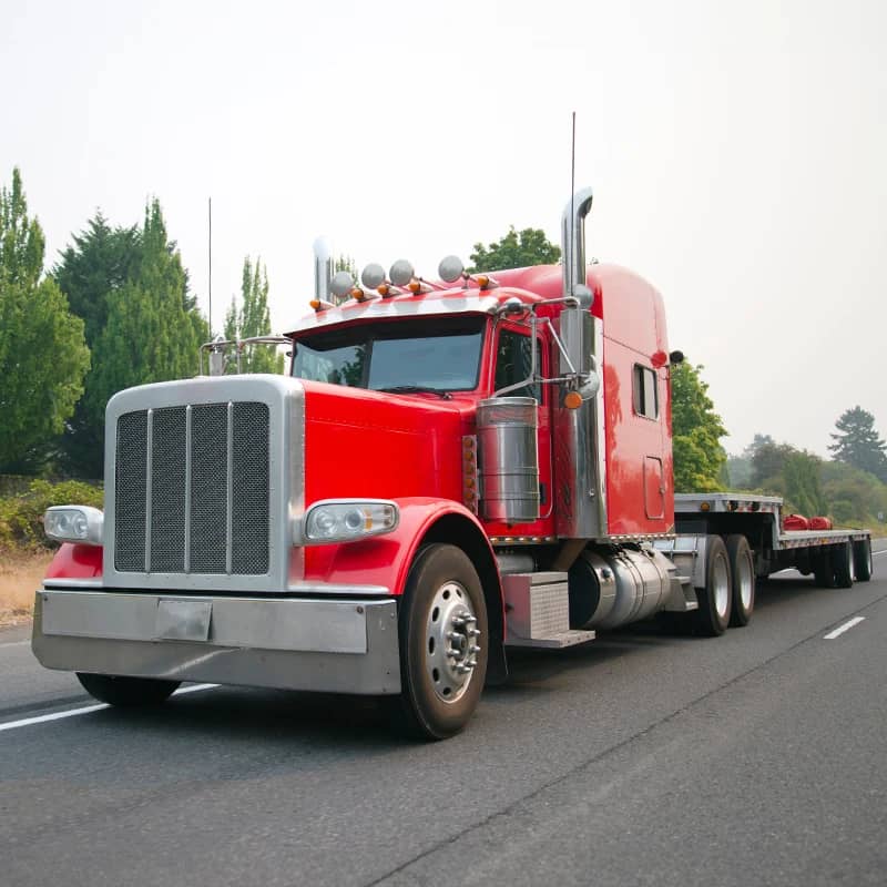 Red semi truck with step deck trailer on the road.