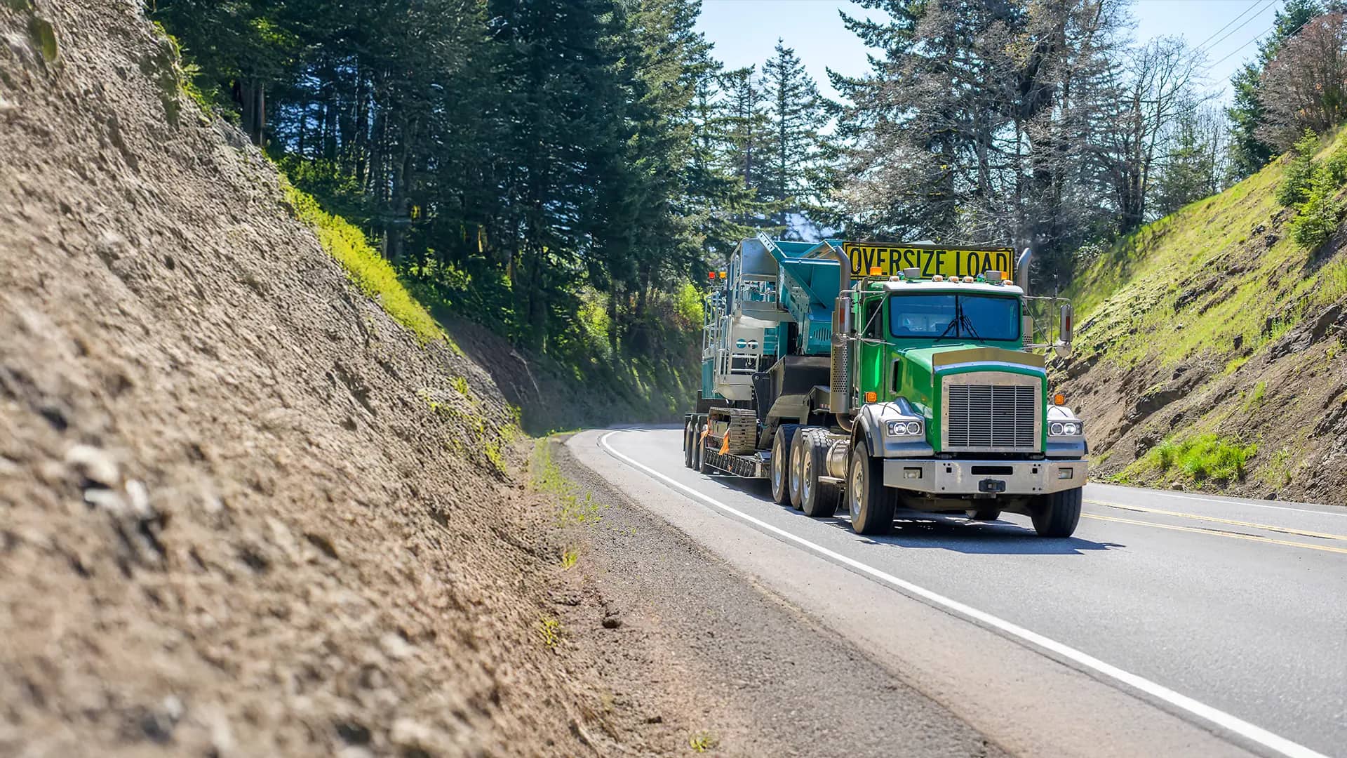 Heavy haul semi truck caring machinery on a highway in the mountains.