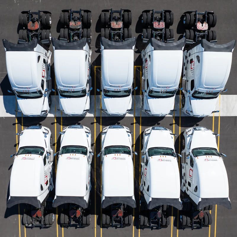 The image presents a top-down aerial view of a fleet of identical white trucks neatly parked in a formation that maximizes space efficiency. Each truck features the "SCHWARZ LOGISTICS" logo on the side, indicating that they belong to the same logistics company.