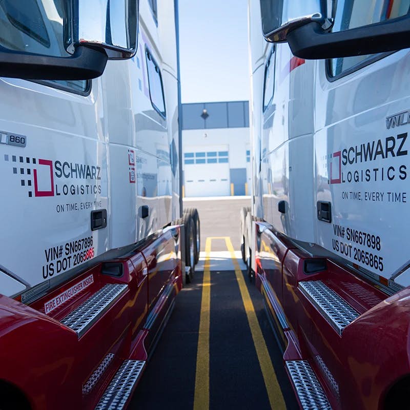 Two commercial trucks parked side by side, with the camera positioned in the narrow space between them, capturing a symmetric view.