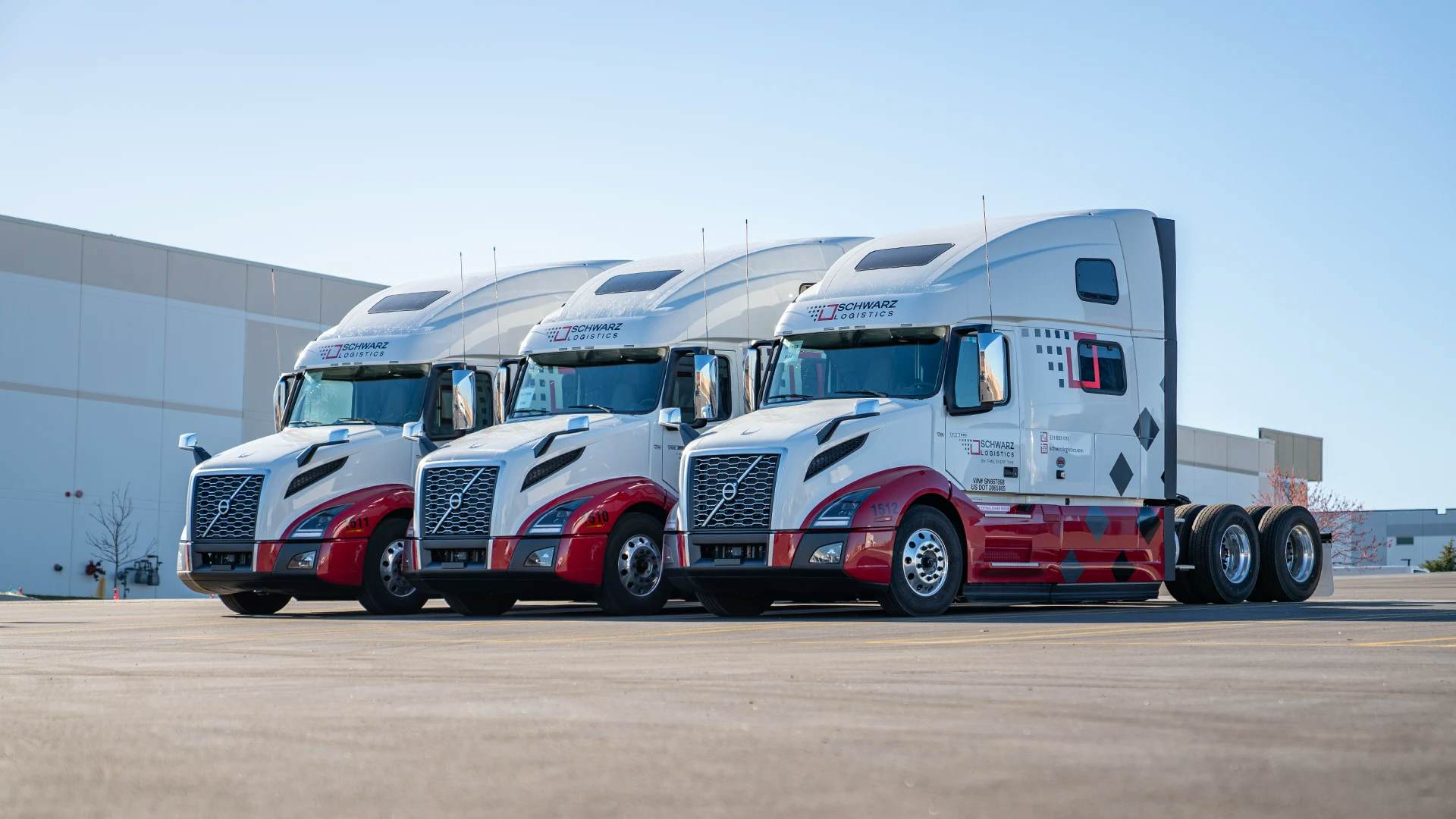 Three modern white semi-trucks with red and gray accents, branded 'SCHWARZ LOGISTICS', are parked side by side in front of a large industrial building, reflecting a fleet-ready position under a clear blue sky.