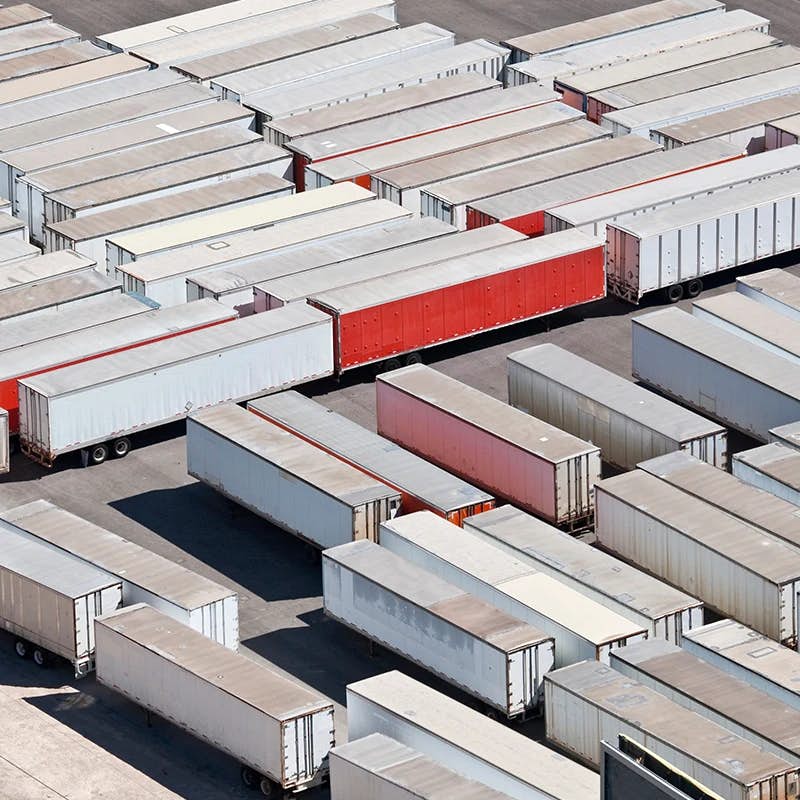 An aerial view of a large parking area filled with neatly arranged rows of trailers in various shades of white, gray, and red, ready for transport or storage.
