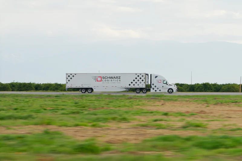 A commercial semi-truck with a trailer emblazoned with "SCHWARZ LOGISTICS" driving along a road.