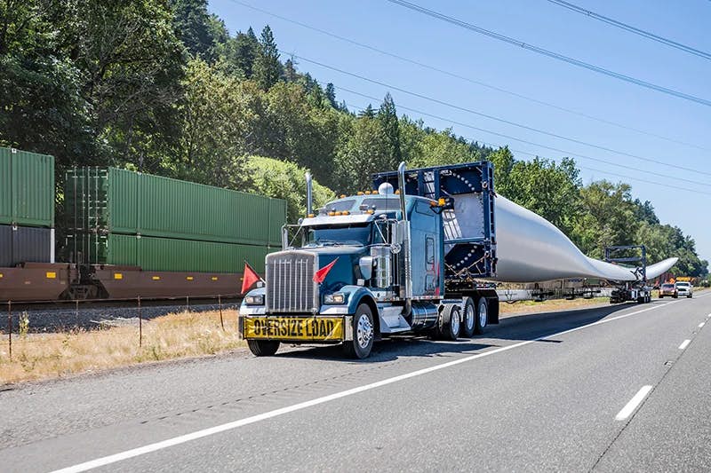 A specialized transportation scenario where a large commercial truck is hauling an oversized wind turbine blade.