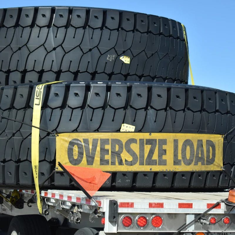 Trailer with stacked large tires and "OVERSIZE LOAD" sign.