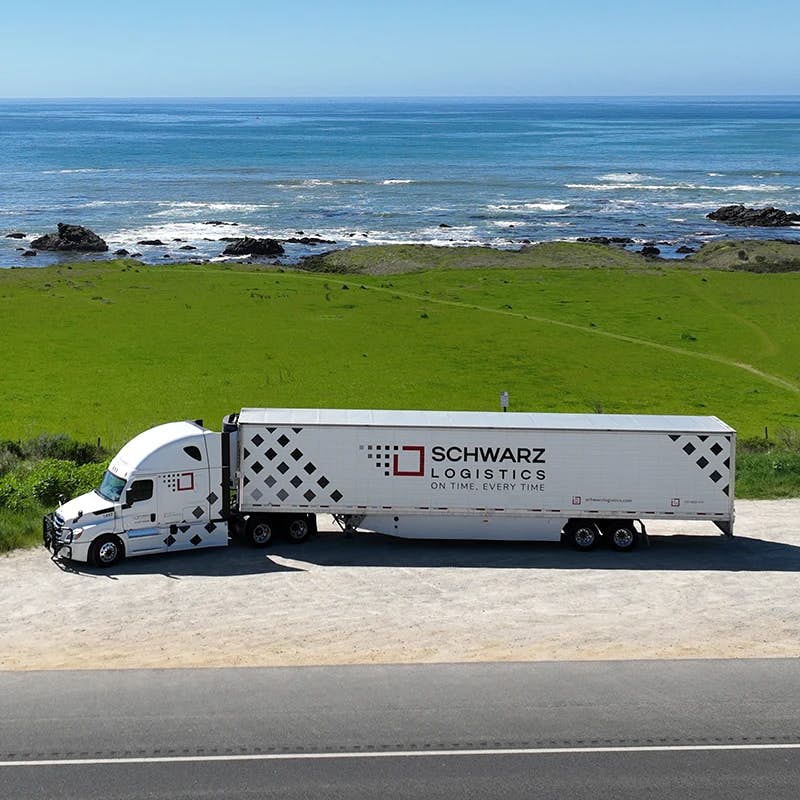 A semi-trailer truck from the "Schwarz Logistics" company parked near a scenic coastal area.