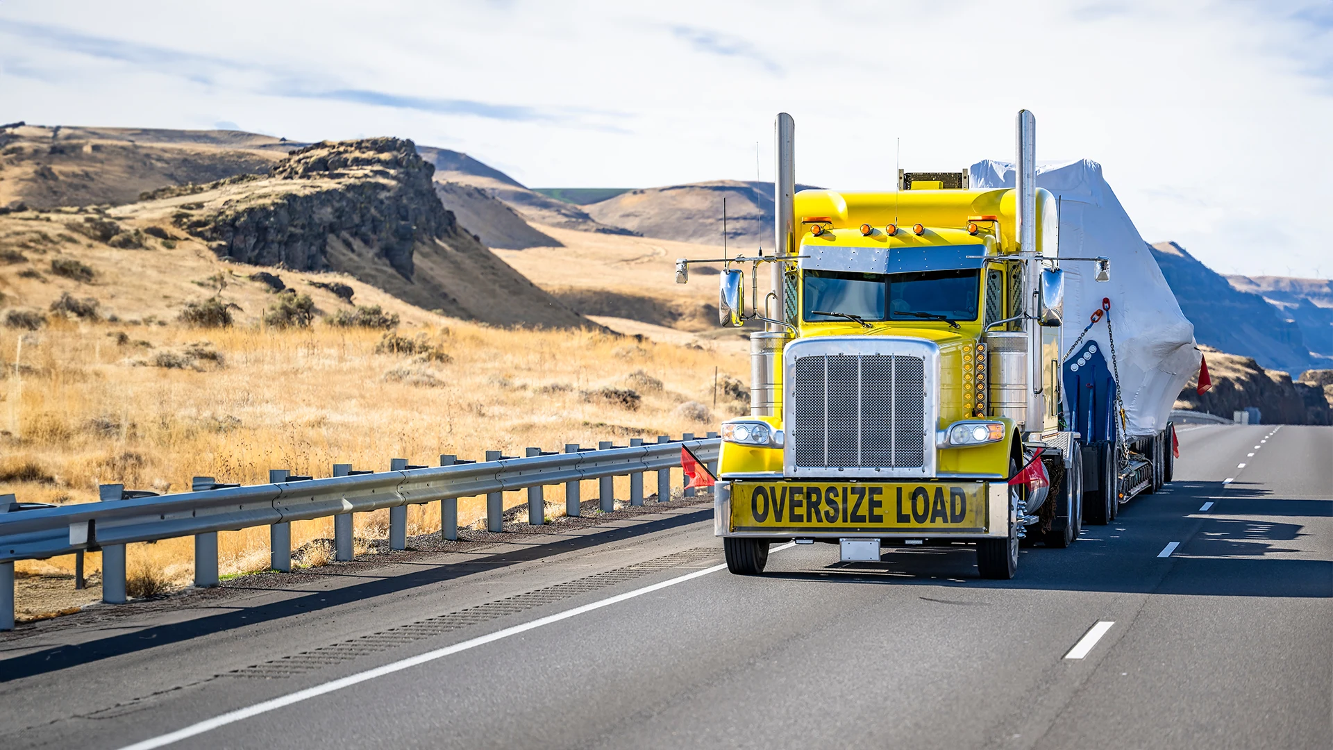 Yellow truck with "OVERSIZE LOAD" banner on a desert highway.