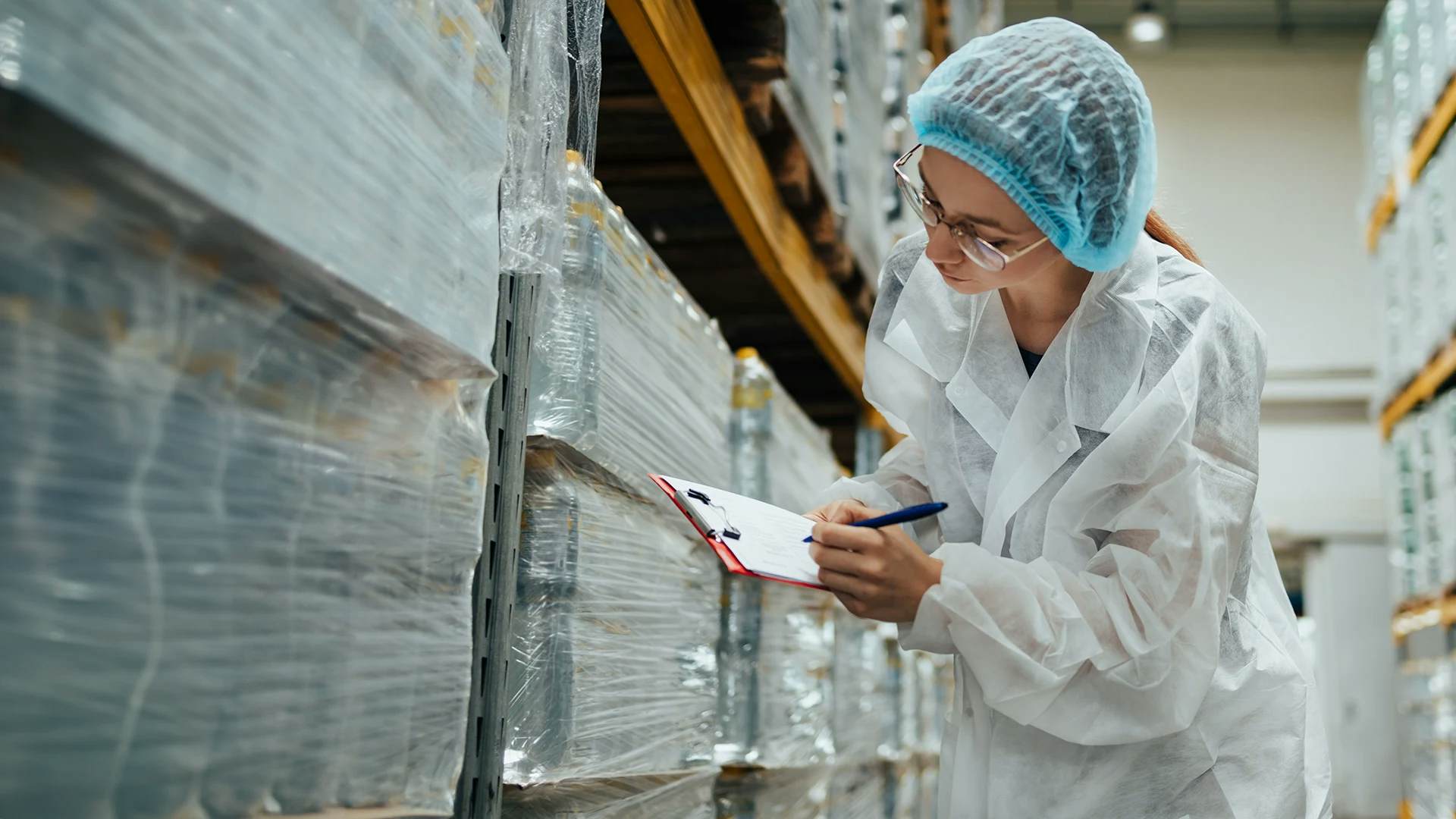 Worker in lab coat checking inventory in a pharmaceutical warehouse.