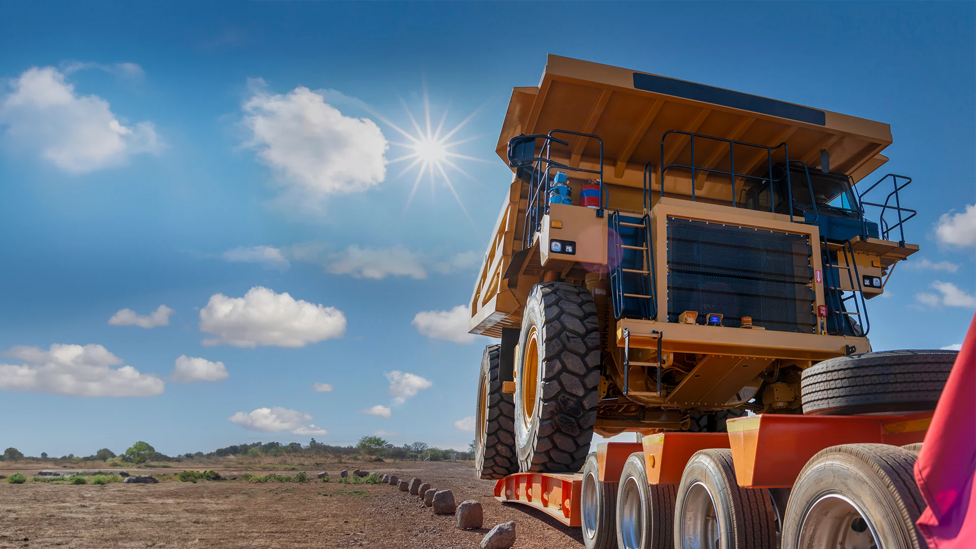 Large mining truck on a RGN trailer, sunny sky, dry landscape.